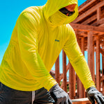 Man wearing a hi-vis yellow GOBI Helio UPF Sun Hoodie with hood and built-in face cover pulled up at a construction site, with wood framing in the background.